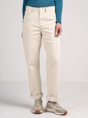 A person wearing off-white straight-leg jeans with rolled cuffs, paired with a blue and white striped long-sleeve shirt and beige sneakers, shown from the waist down against a light gray studio background.