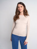 A woman modeling a light beige long-sleeve crewneck sweater paired with blue jeans, photographed against a neutral light gray studio background.