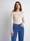 A woman modeling a beige long-sleeve crewneck top paired with blue jeans, standing against a light gray studio background.